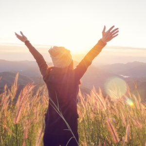 Kvinna sträcker armarna mot himlen i solnedgång. Utveckling av arbetsmiljö, samarbete, psykisk hälsa och motivation. Self-Determination Theory SDT, Inner Development Goals, IDG. Organisation, team, arbetsuppgifter, implementering, vardagsträning, grupparbete, Medveten Arbetsplats